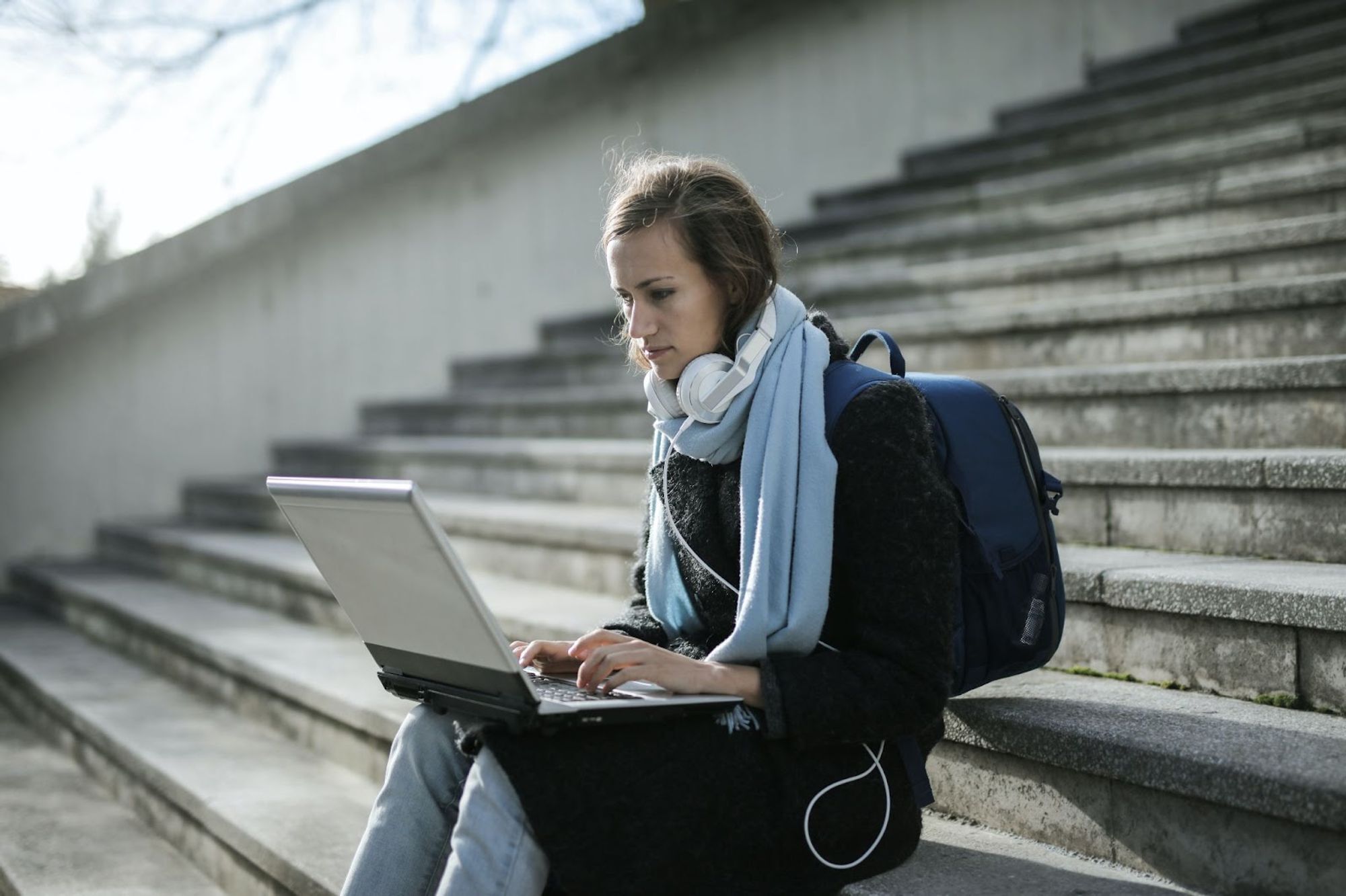 Femme assise sur des escaliers extérieurs en hiver avec sac à dos et ordinateur