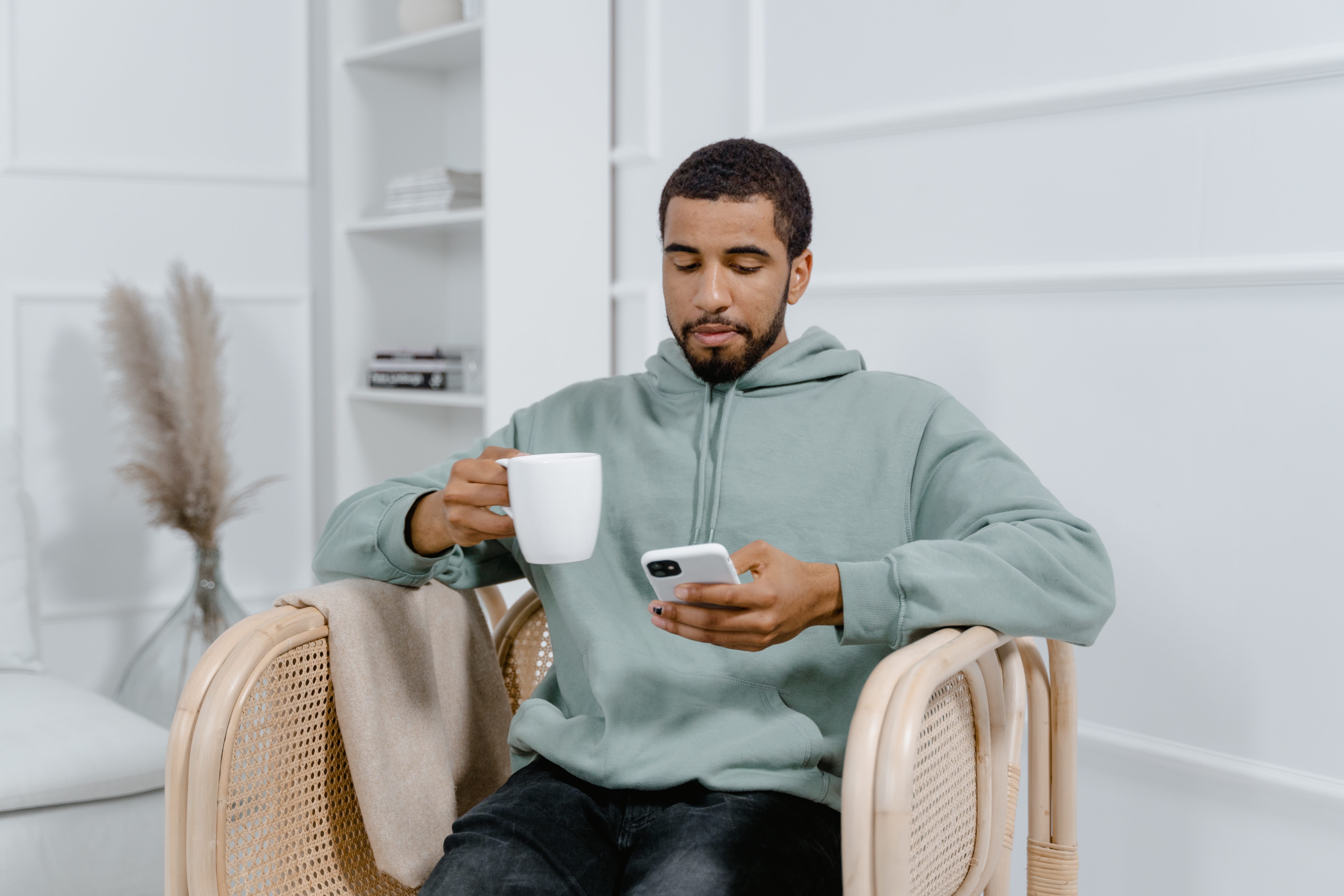 Homme sur un fauteuil en osier avec son téléphone et un café